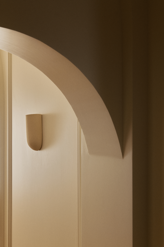 Mur beige avec une applique murale en forme de demi-cylindre et un arc blanc sur le plafond.