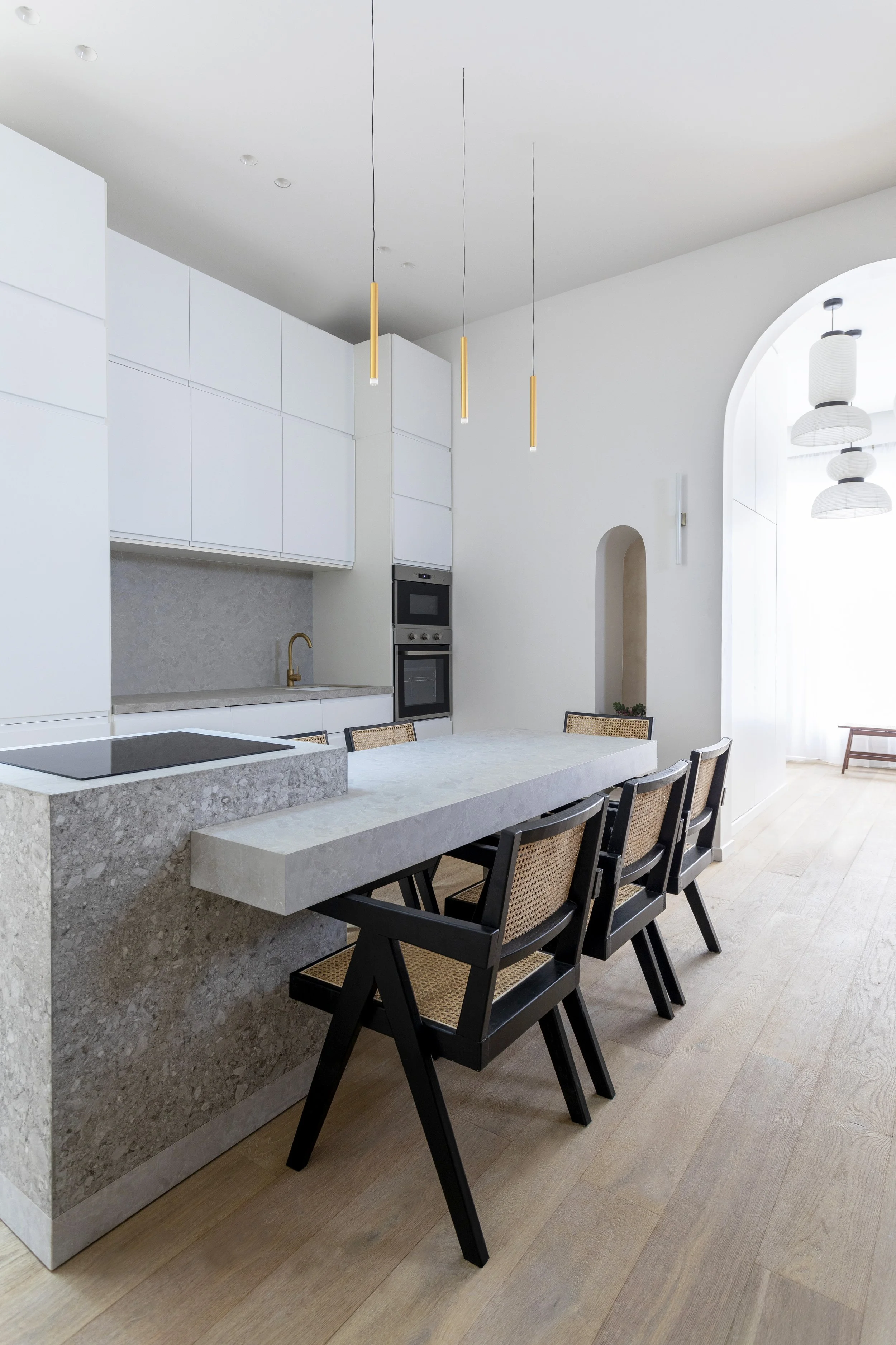 Cuisine moderne avec un comptoir en pierre et des chaises en bois et canevas, suspendus avec des lampes au plafond, armoire blanche et mur blanc.