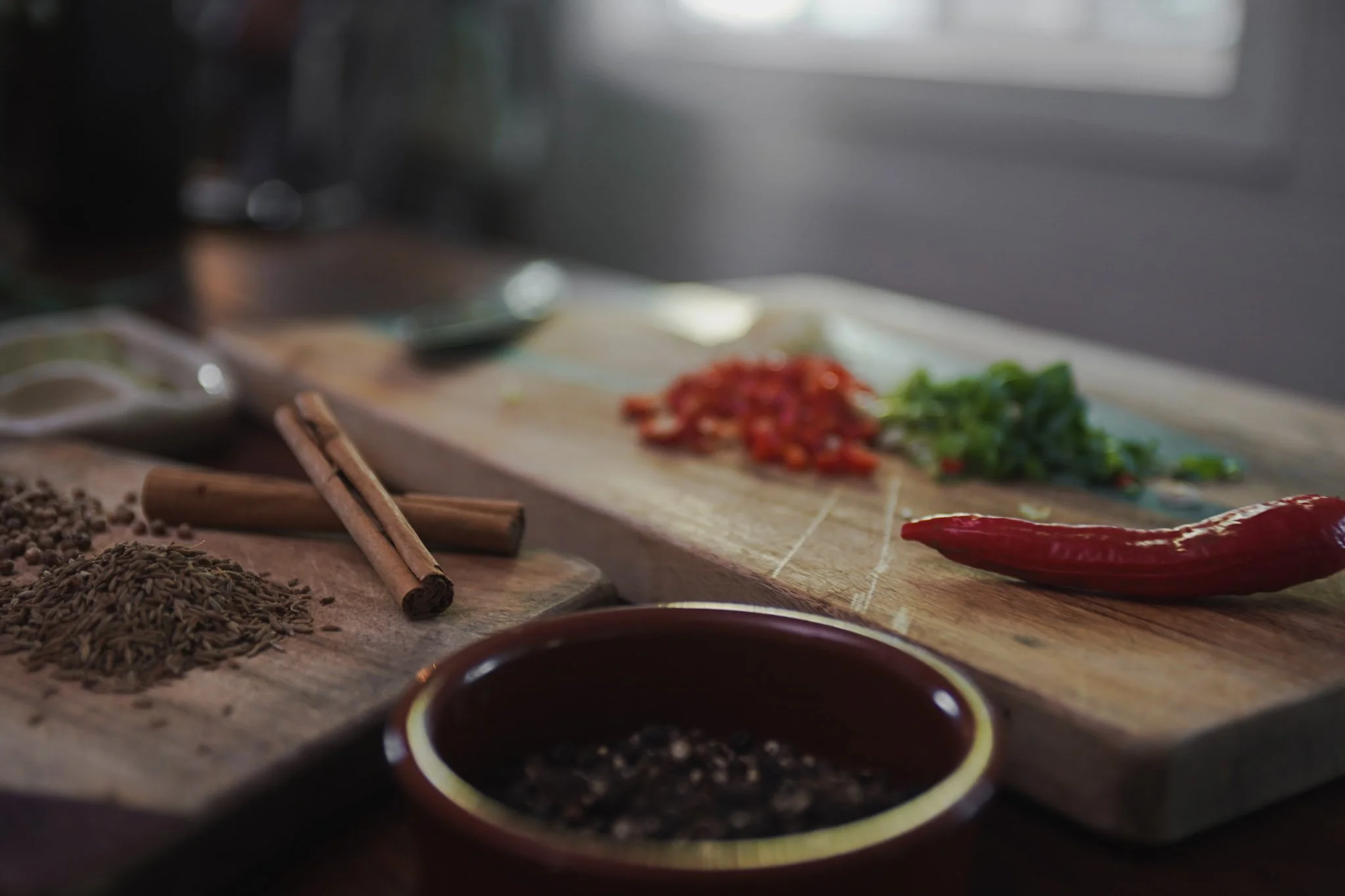 Close-up of culinary ingredients on a kitchen counter, including spices, a red chili pepper, and chopped vegetables on a cutting board.