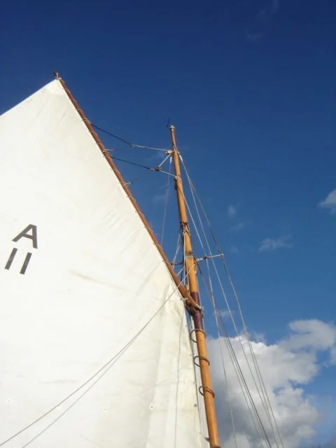 Close-up of a sailboat's mast and sail against a partly cloudy blue sky.