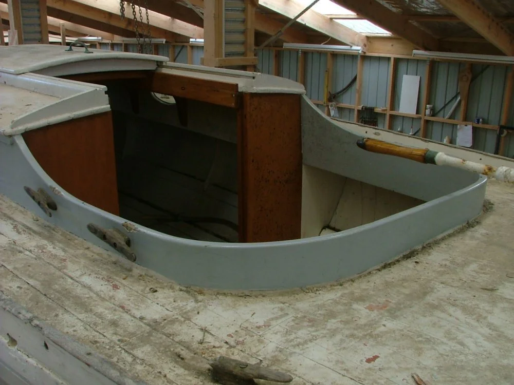 A partially assembled boat inside a workshop with wooden and metal walls and a sloped roof.