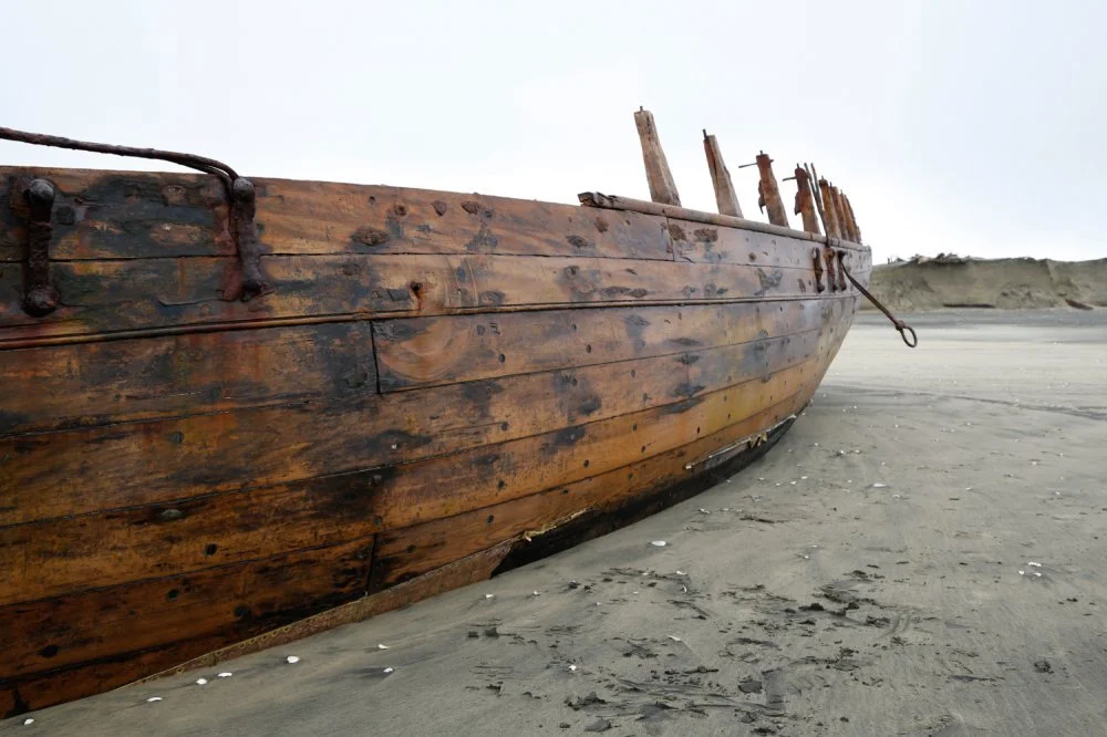 An old wooden boat resting on a sandy beach with a cloudy sky in the background.