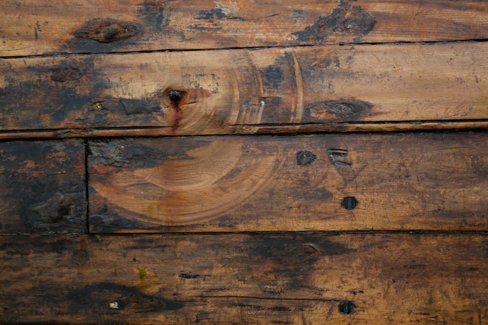 Close-up of a wooden surface with visible grain, knots, and imperfections.