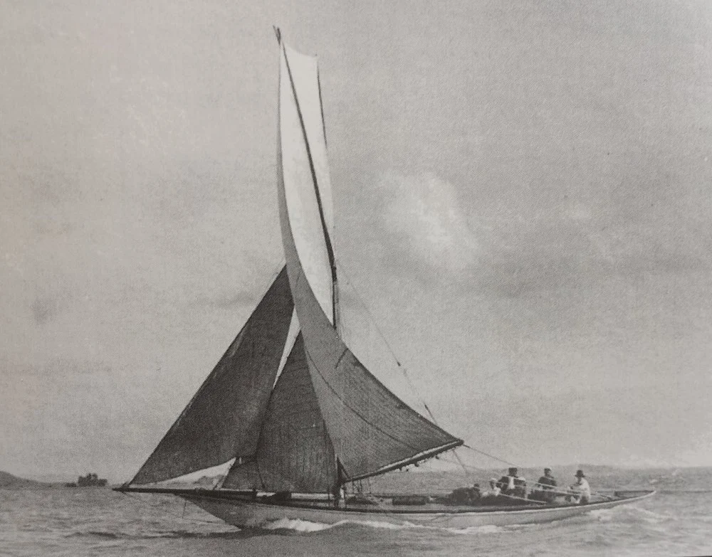 A sailboat with large sails on the water, with four people onboard, cruising in a cloudy sky.