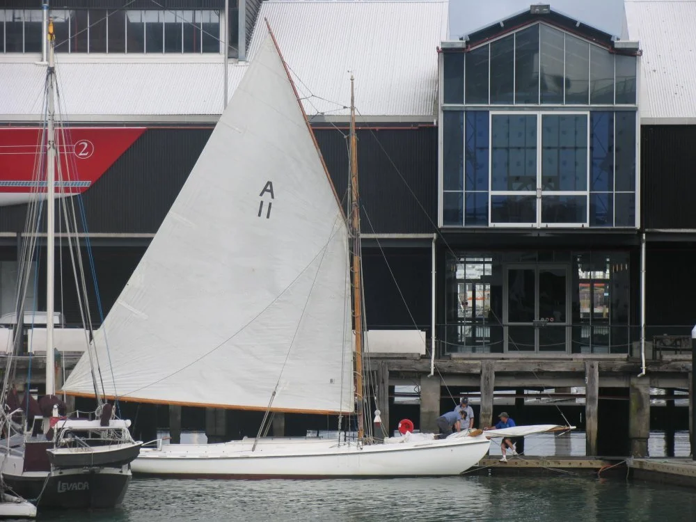 A sailboat docked at a marina with a modern black and glass building in the background.