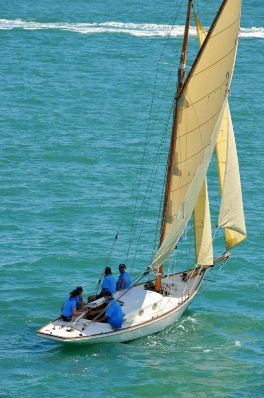 A sailboat with four people on board sailing on the water.