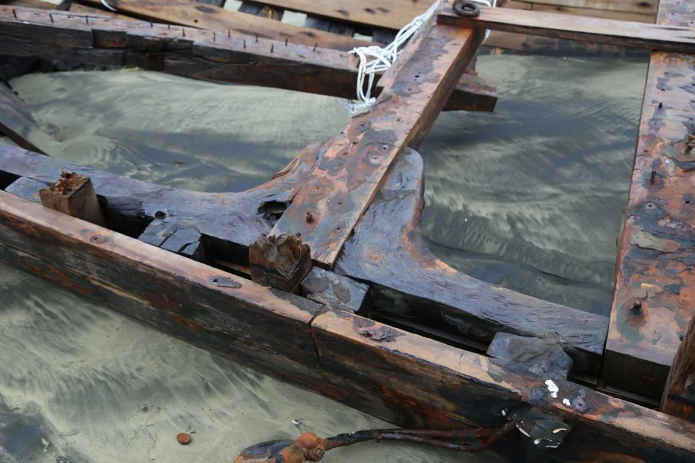 A weathered, partially submerged wooden boat frame with visible signs of decay and rusted nails, floating in water.