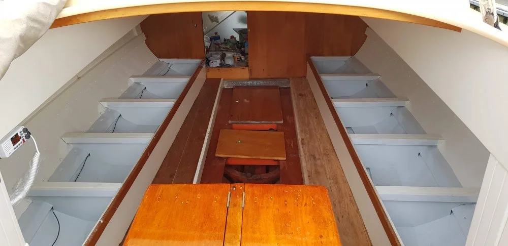 Interior view of a boat under renovation with empty refrigeration units on each side and a wooden floor and cabinets.