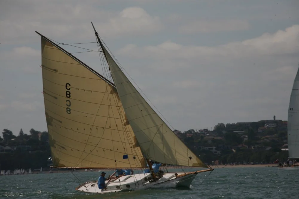A sailboat with gold-colored sails sailing on the water during daytime with cloudy sky.