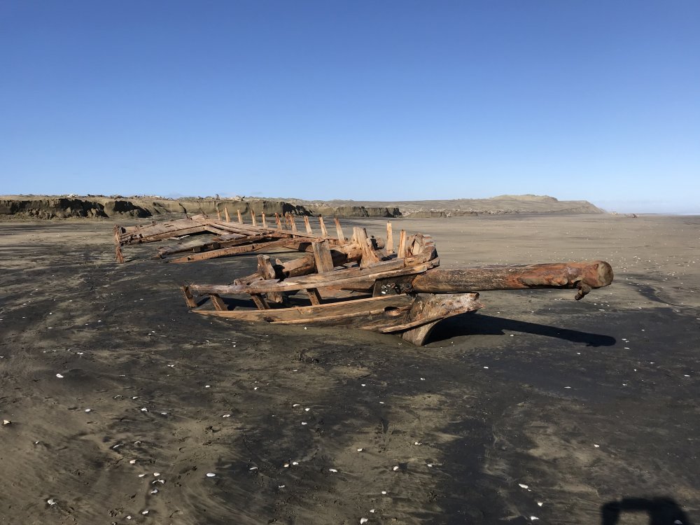 Old, wrecked wooden shipwreck on a sandy beach under a clear blue sky.