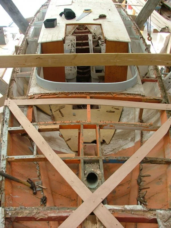 View of a boat under construction or repair, showing a partially built hull with wooden beams and tools placed on the top deck.
