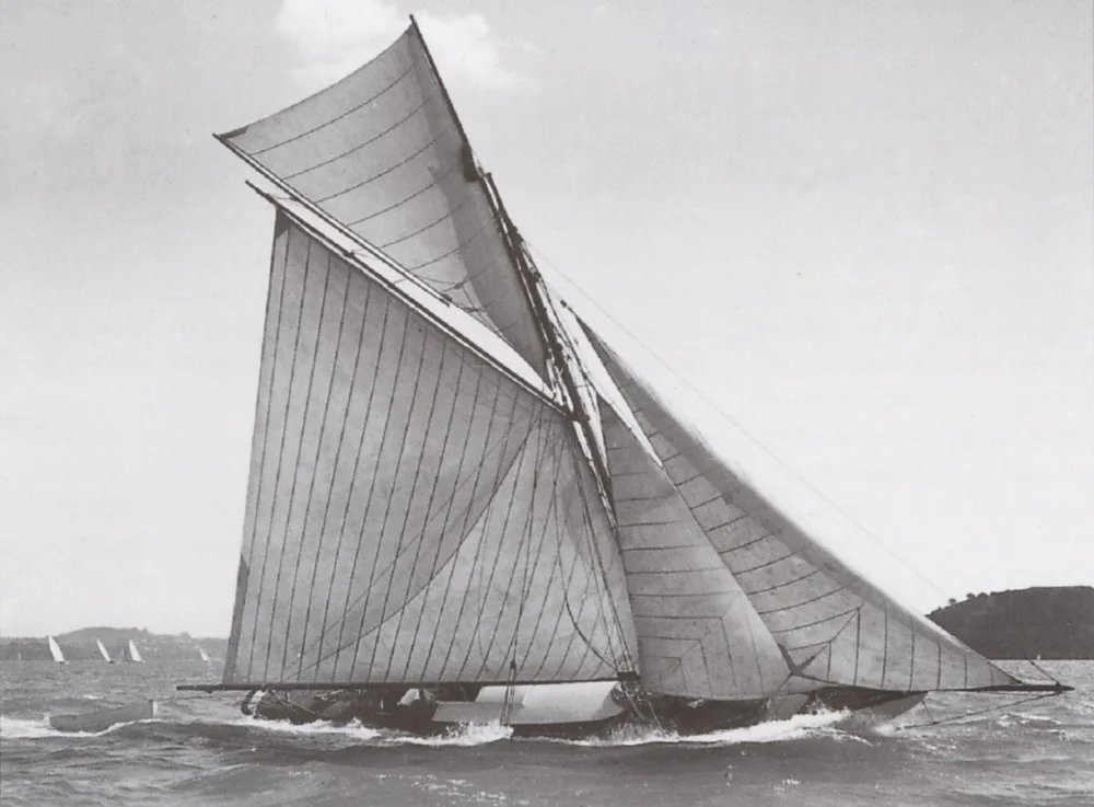A sailboat with large sails on the water with a distant shoreline in the background.