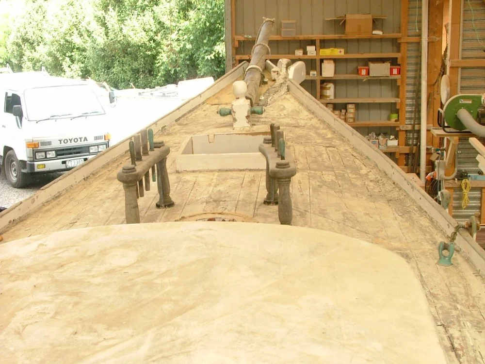Wooden boat under construction in a woodworking shop with tools and storage shelves
