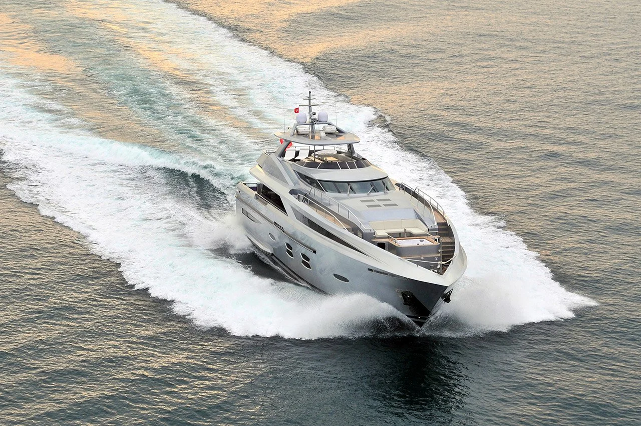 A large, modern white yacht cruising through the water at sunset, creating a wake behind it.