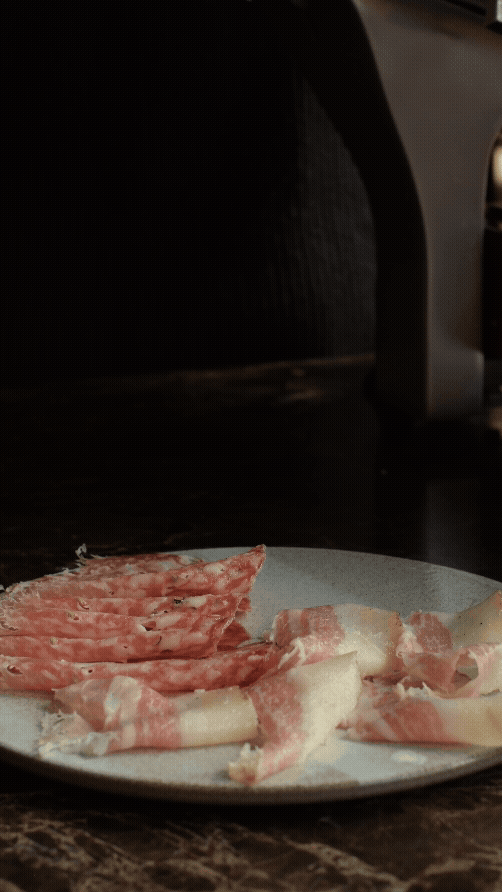 Tynne skiver av rått bacon på en hvit tallerken på et kjøkken.