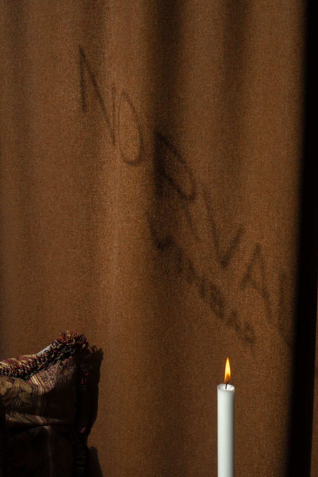 Tegning av en kvinne og en mann som kysser, som er laget med stearinlys på en vegg, med en tent stearinlys foran.