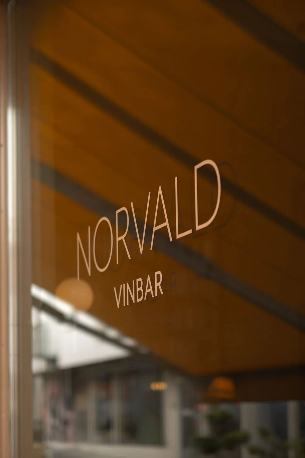 Skilt med teksten 'NORVALD VINBAR' i glass foran en bygning med treverkstak.