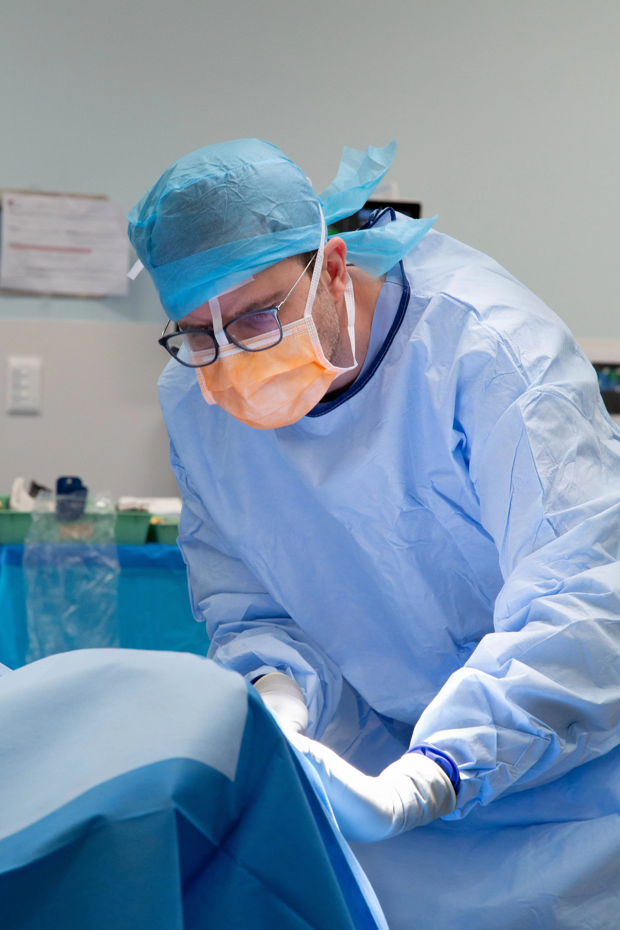 Medical professional in surgical attire, including blue cap, mask, and gown, performing a procedure in a sterile environment