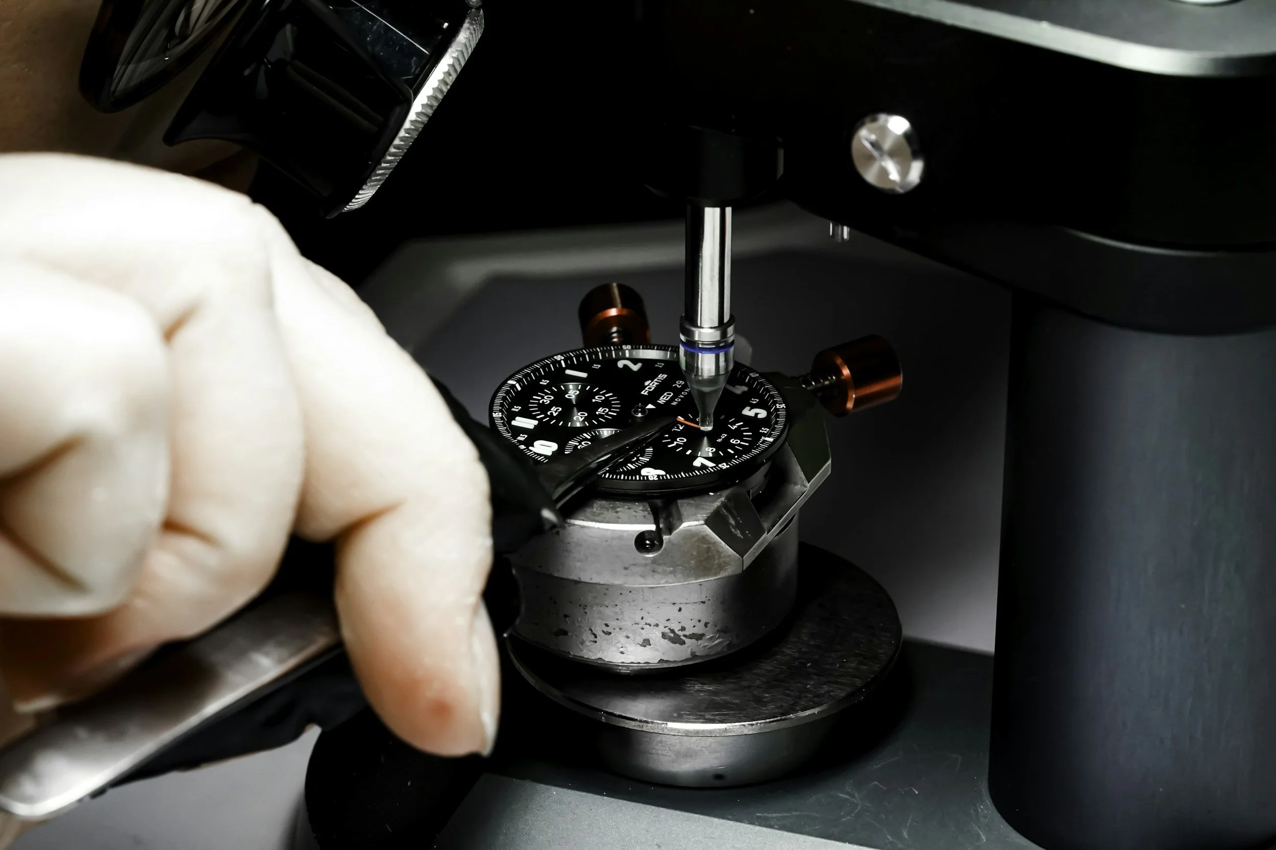A person adjusting a dial on a scientific instrument called a spectrometer or a similar device used for precise measurements, with a focus on the dial and hand, and the instrument's components visible in the background.