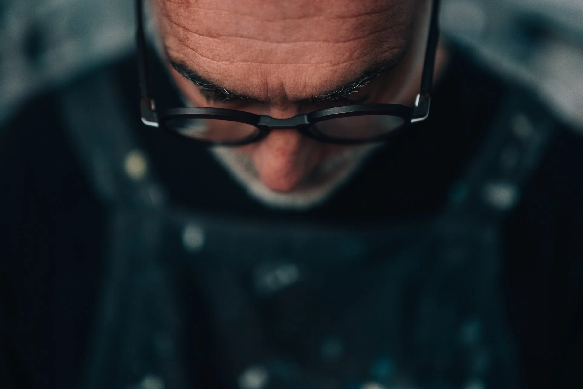 Close-up of a person's face looking down, wearing black glasses, with a focus on the forehead and eyebrows.