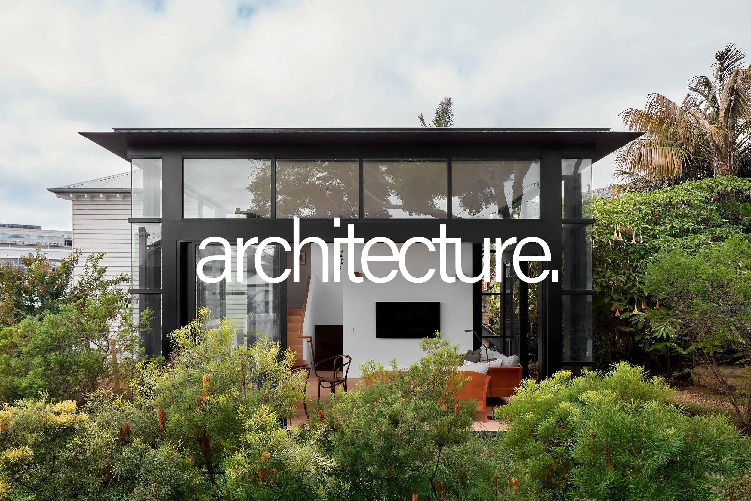 Modern house with large glass windows surrounded by lush greenery and trees.