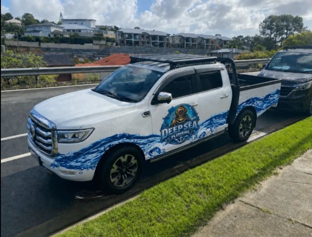 White pickup truck with a Deep Sea Divers logo and blue ocean waves painted on the side, parked on the street.