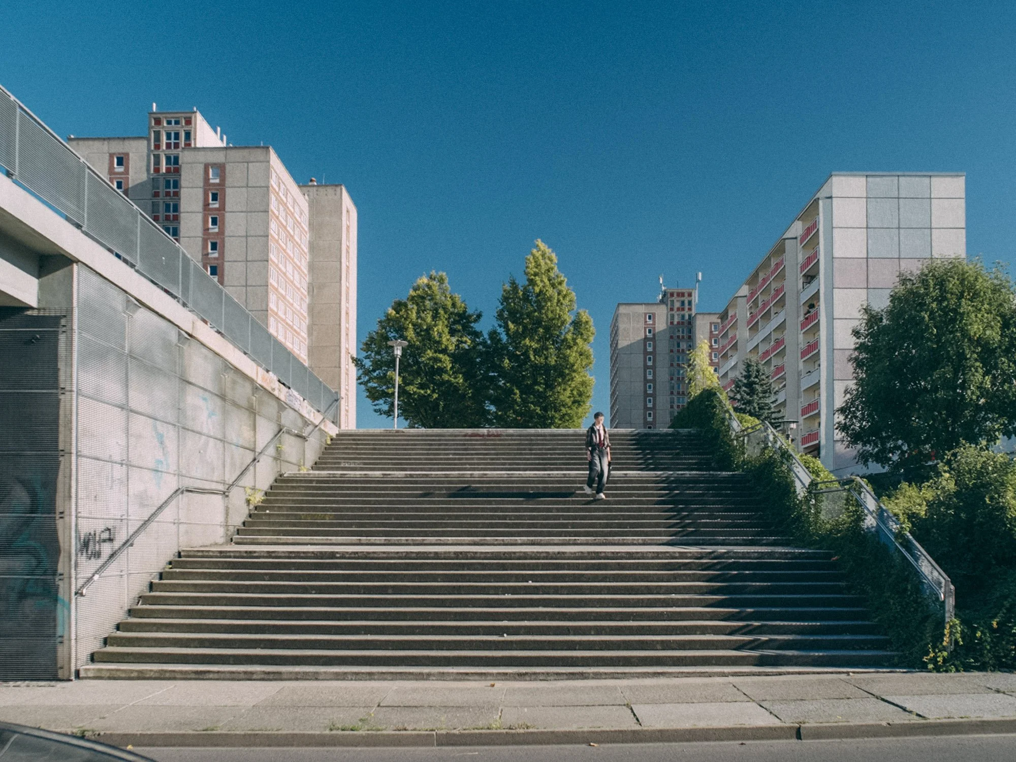 Cityscape with tall buildings, trees, and a staircase with a person walking down, under a clear blue sky.
