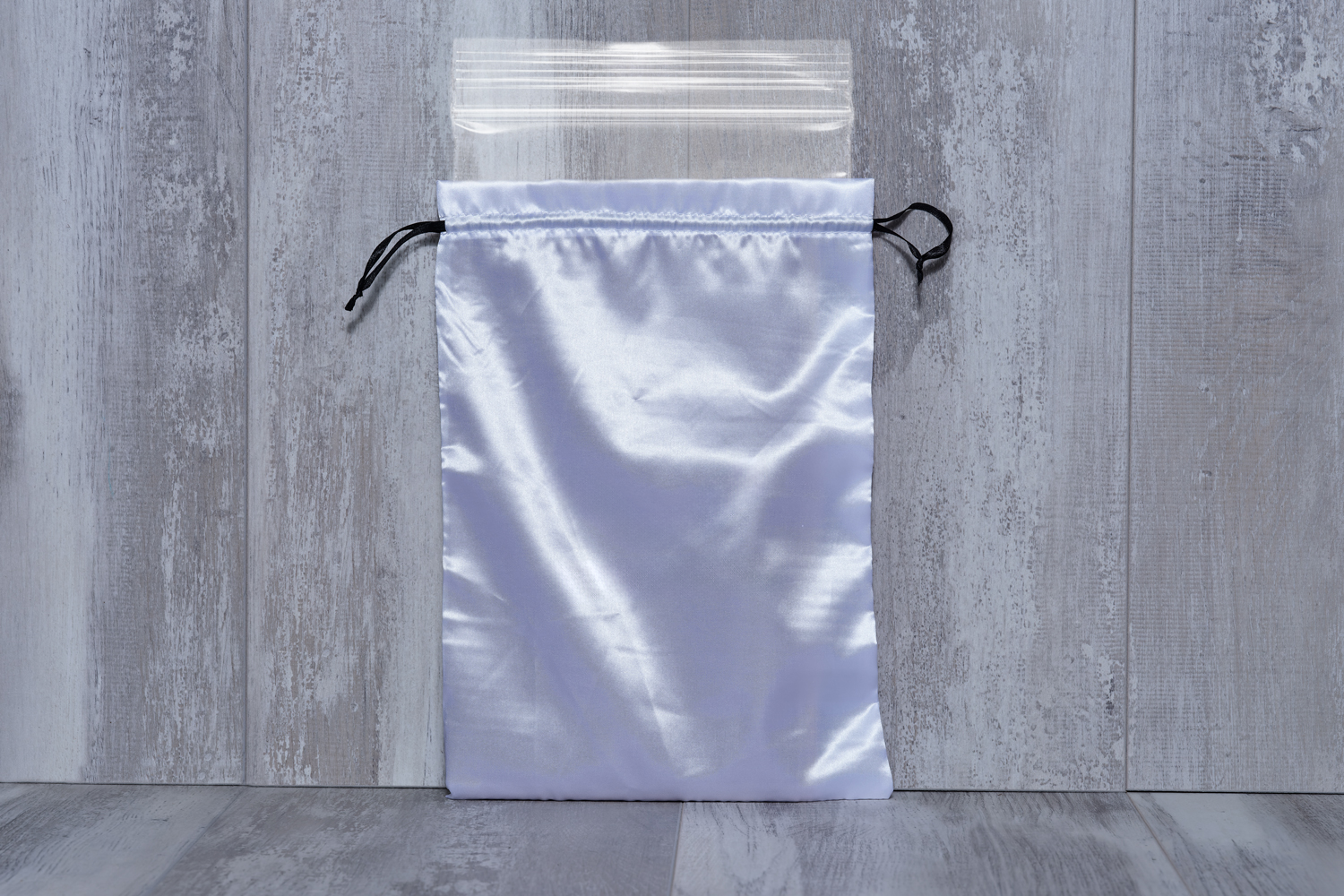A white satin drawstring bag with a pink and black butterfly logo and the words 'Rap in Memories' on it, placed against a light gray wooden background.