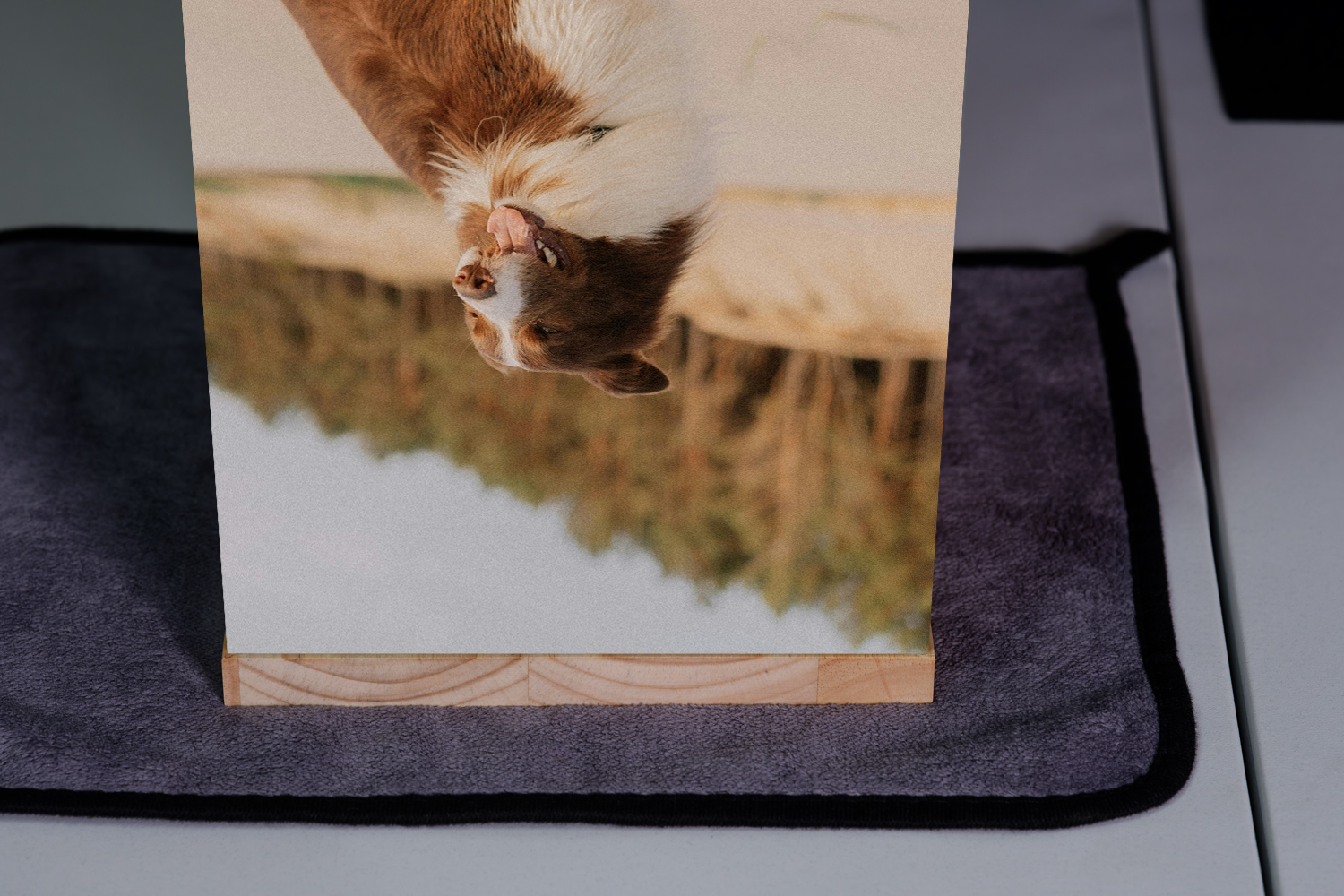 A printed picture of a waterfall in a lush green forest, mounted on a wooden block and placed on a gray cloth surface.