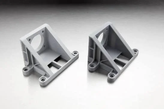 Two gray plastic mounting brackets with holes and slots, placed on a flat surface.