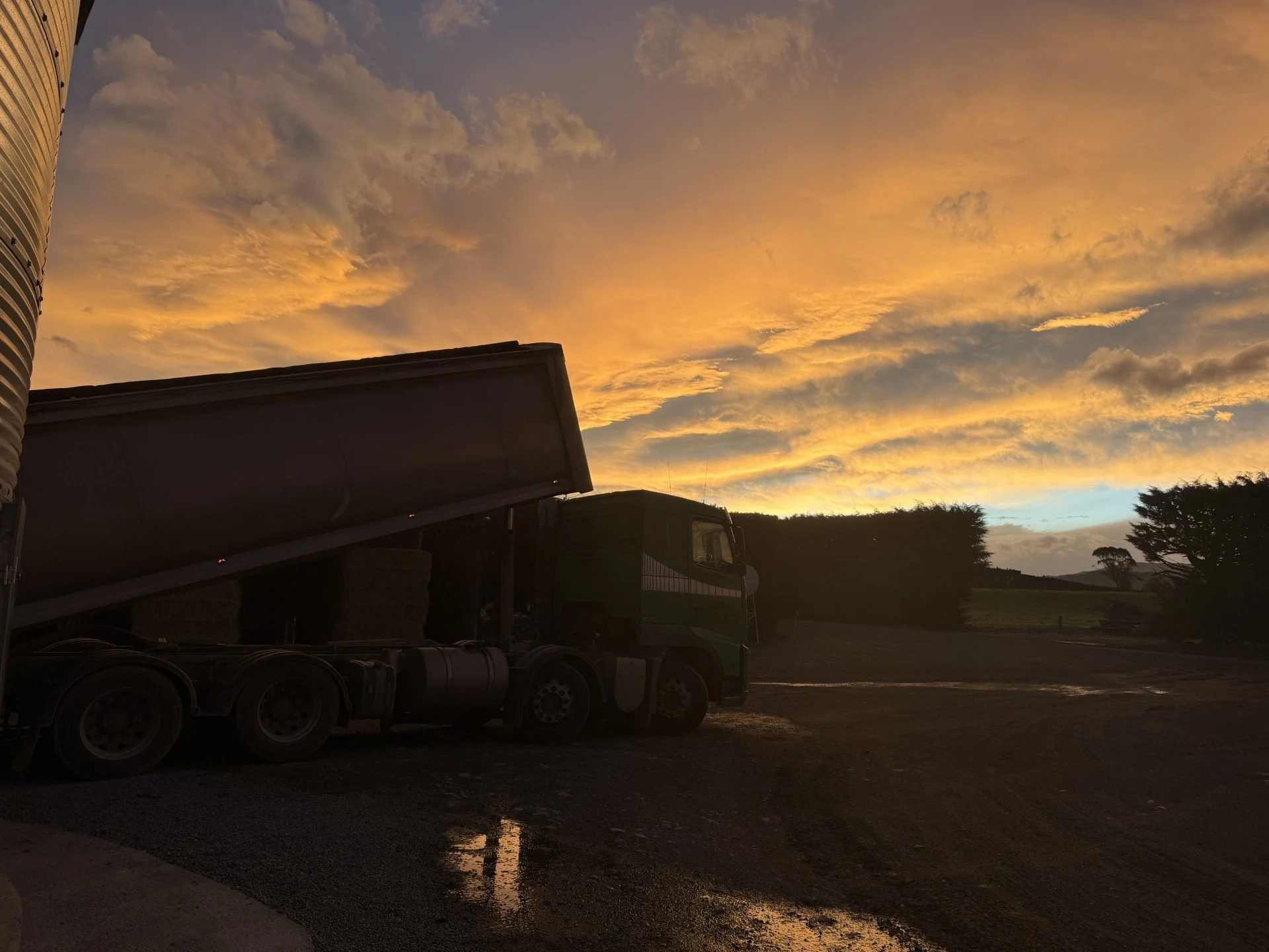 A truck parked outside during sunset with a colorful sky and some trees in the background.