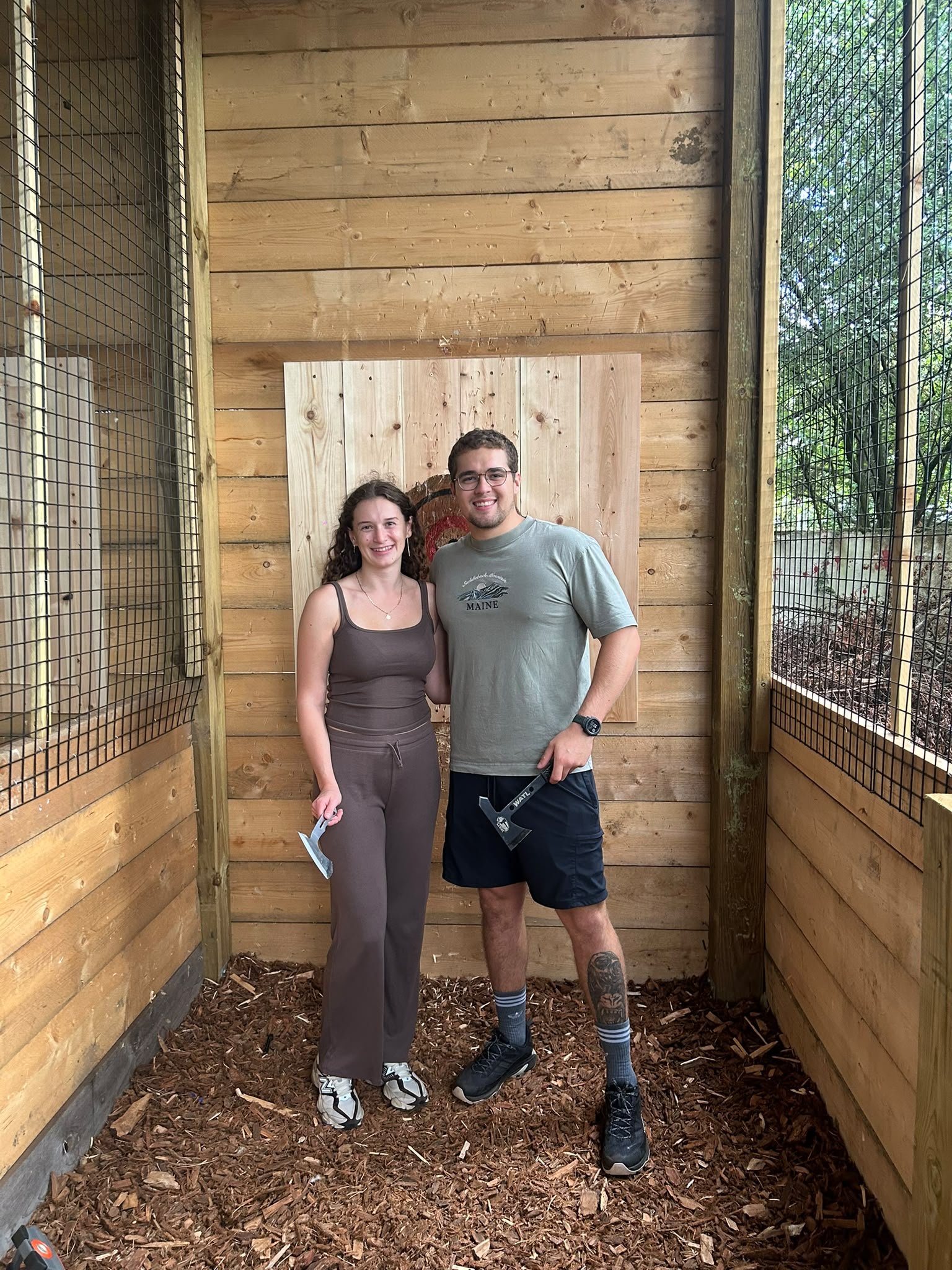 Two guests posing beside the wooden target wall at Bermuda Blades