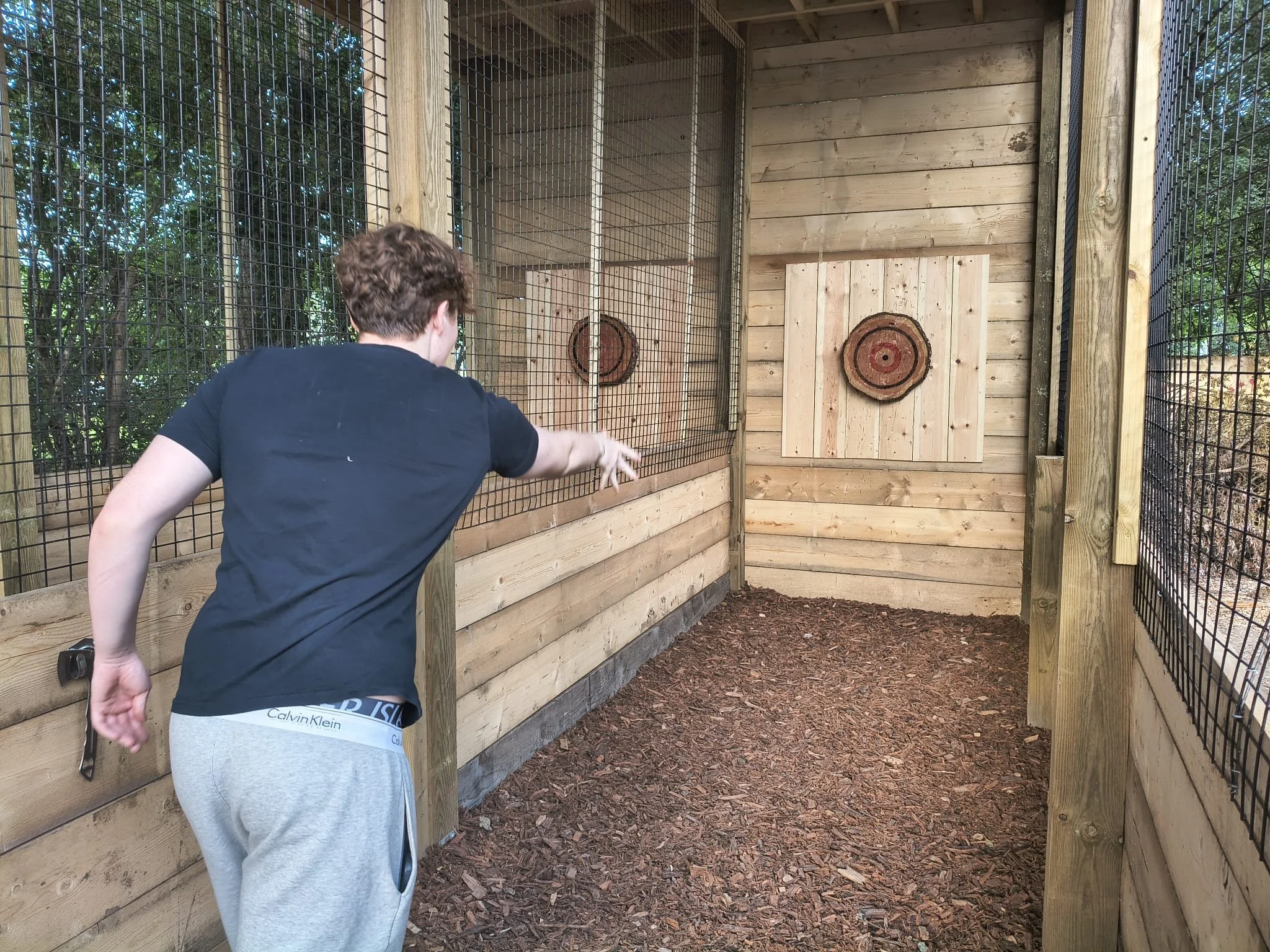 A customer throwing an axe during a covered outdoor axe throwing session at Bermuda Blades in Henlow, Bedfordshire.