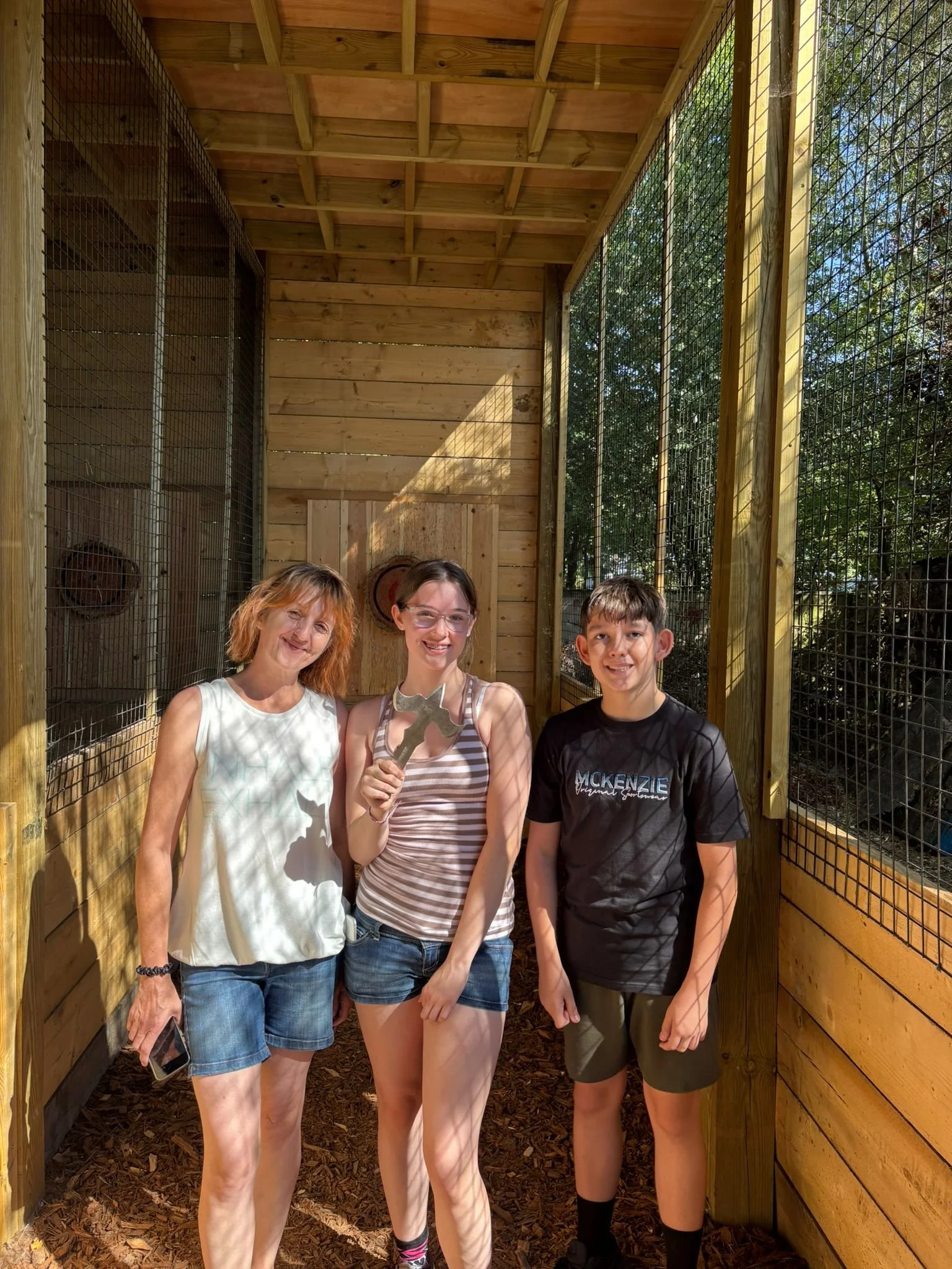 Three guests posing in the covered axe throwing lane at Bermuda Blades