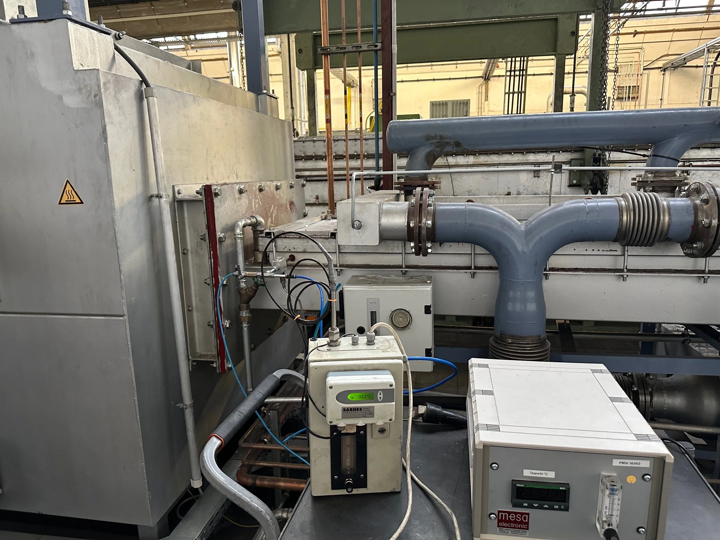 Industrielle technische Einrichtung mit Rohren, Kabeln und Steuergeräten in einem Labor oder Werkstatt. Ein Display zeigt eine Temperatur von -33,3 °C.