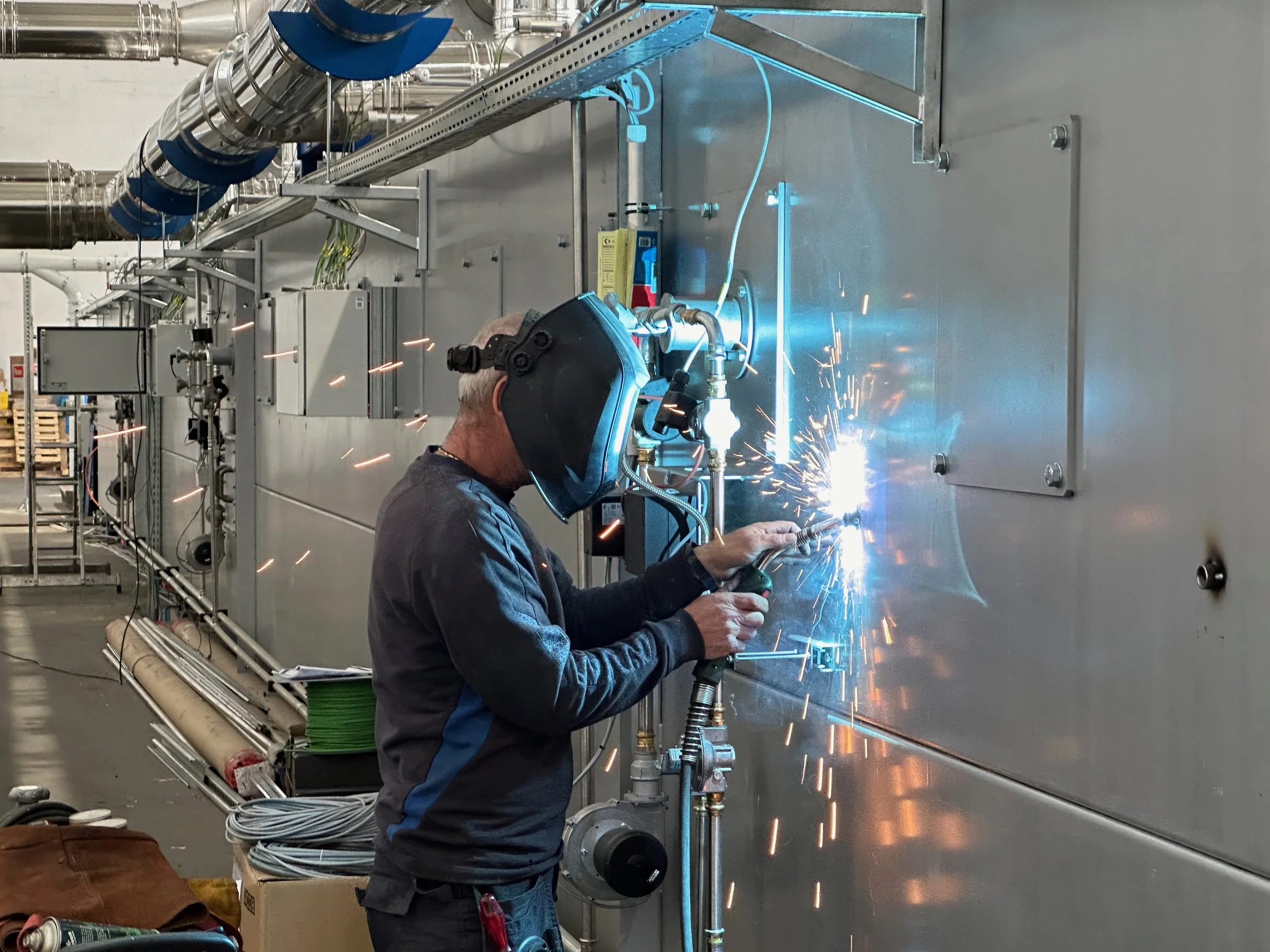 SARNES Techniker schweißt Metallteile in einem industriellen Umfeld, während Funken fliegen.