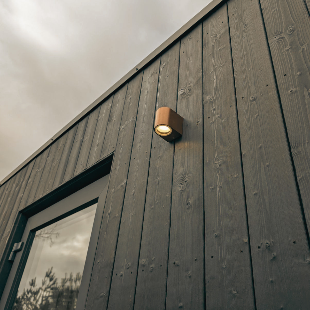 Close-up of an exterior charred sugi ban clad wall with a mounted outdoor light fixture turned on during overcast weather.