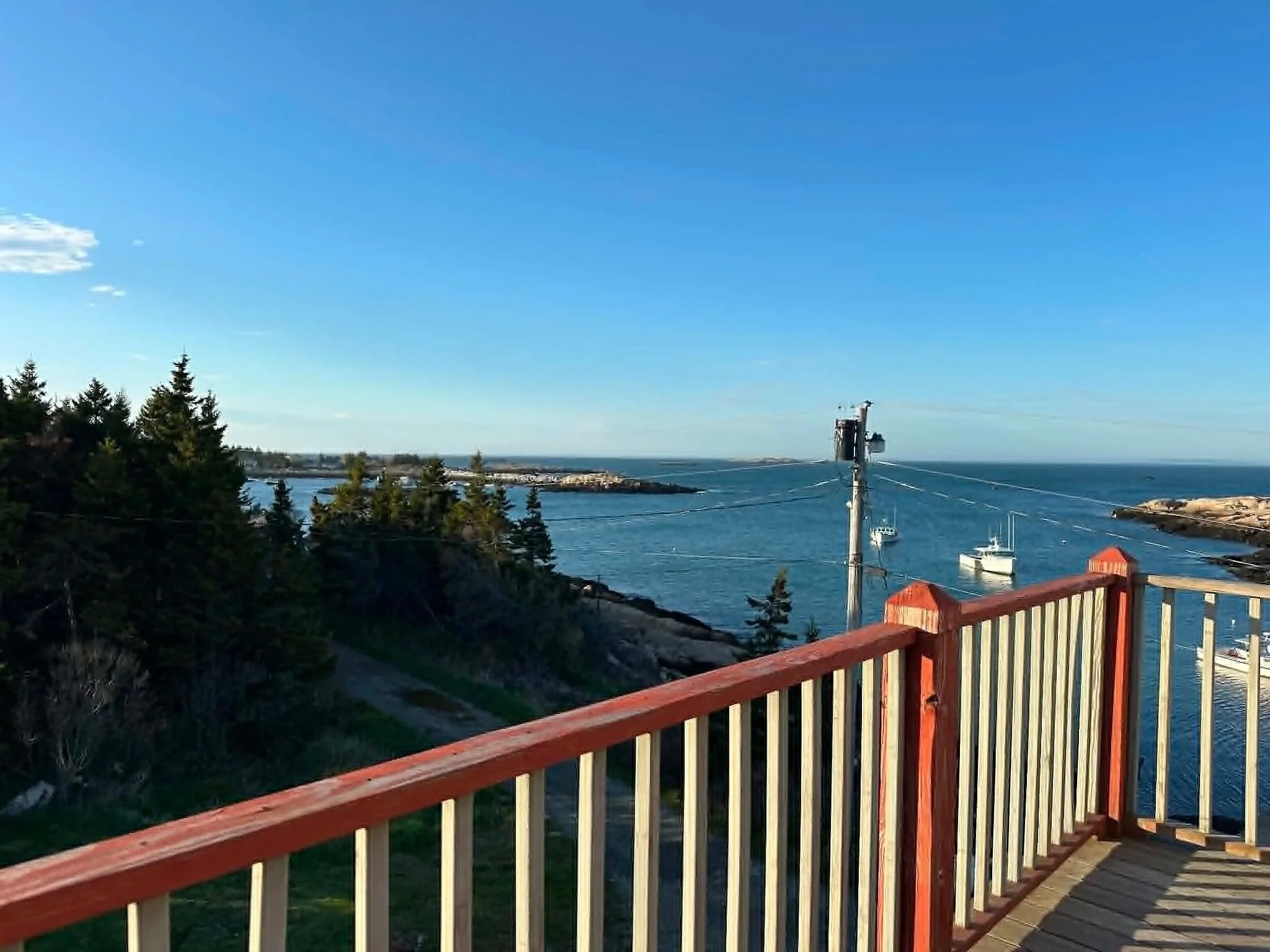 View of a harbor with boats, trees, and a sky with some clouds, seen from a wooden balcony or deck with red and white railings.