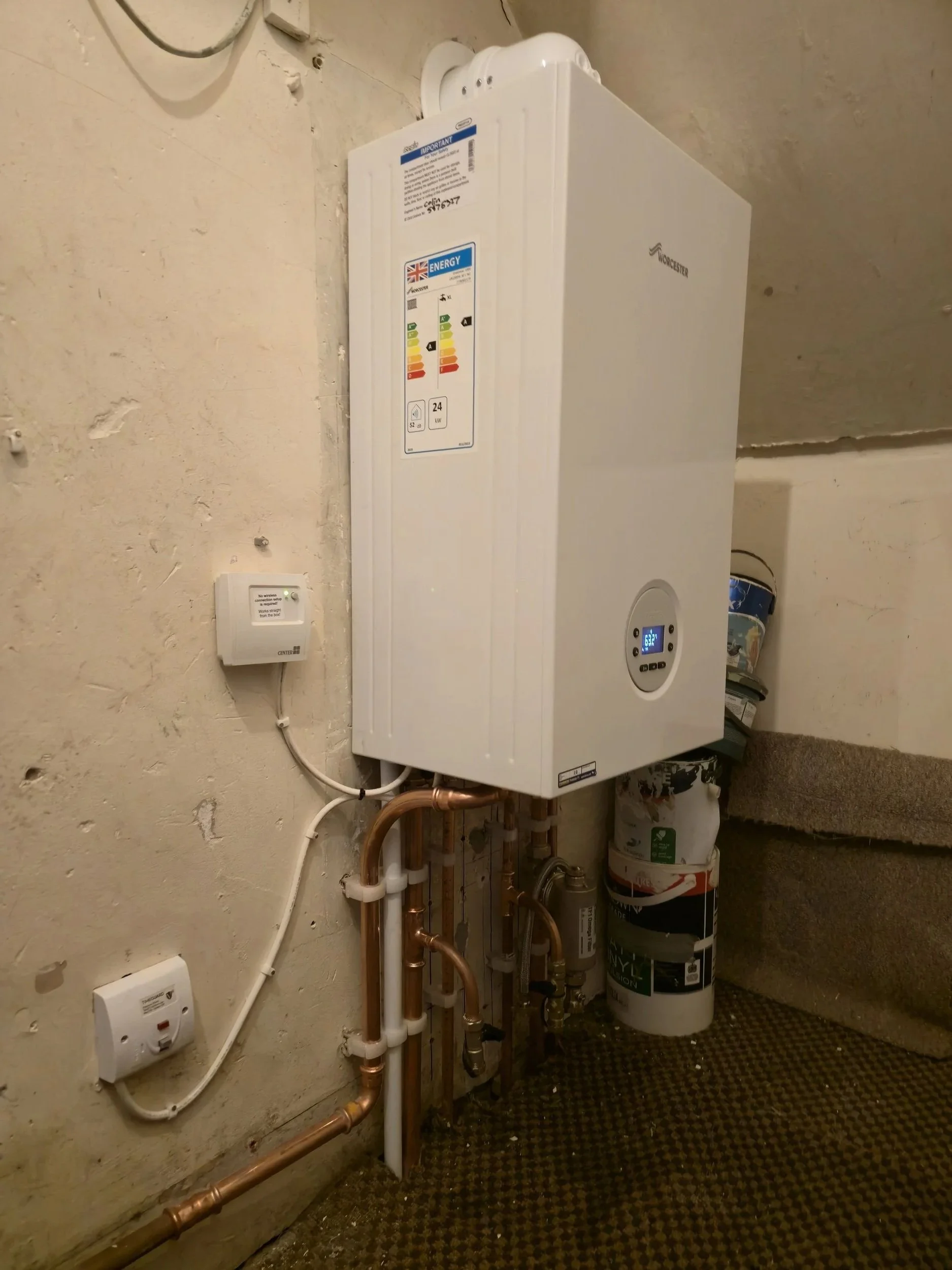 Utility room with a white heater unit mounted on the wall, copper and PVC pipes below it, and various water filters and containers on the floor.