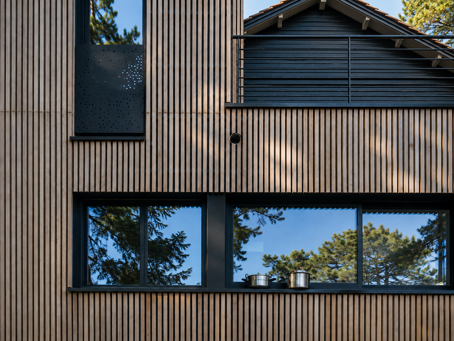 Détail de façade : le bardage en bois naturel vieilli et les menuiseries noires composent une écriture architecturale précise, entre chaleur et rigueur.