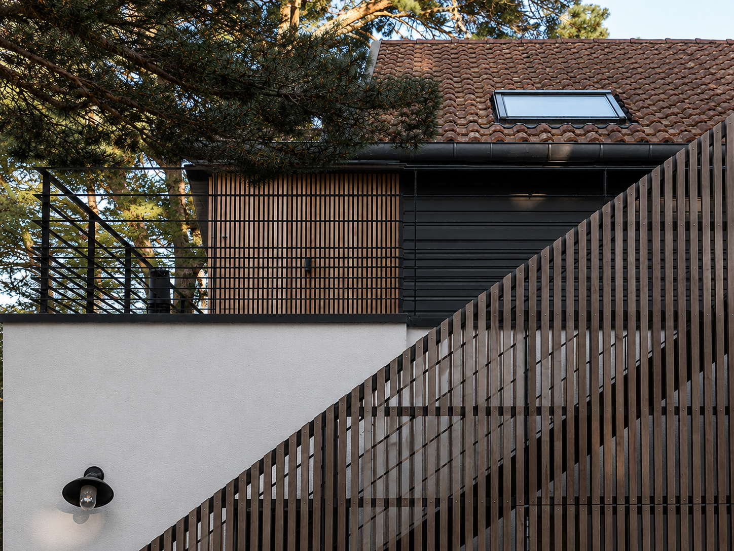 Bardage bois clair, toiture à faible pente et menuiseries noires — une architecture sobre et précise, ancrée dans son environnement boisé.