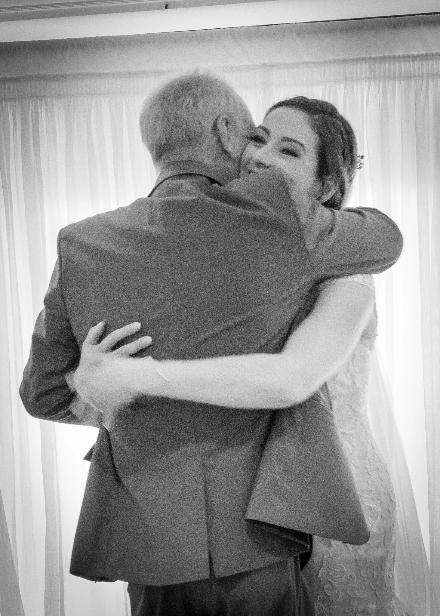 A man and woman are hugging each other in a close embrace, smiling and appearing happy, with just the upper parts of their bodies visible.