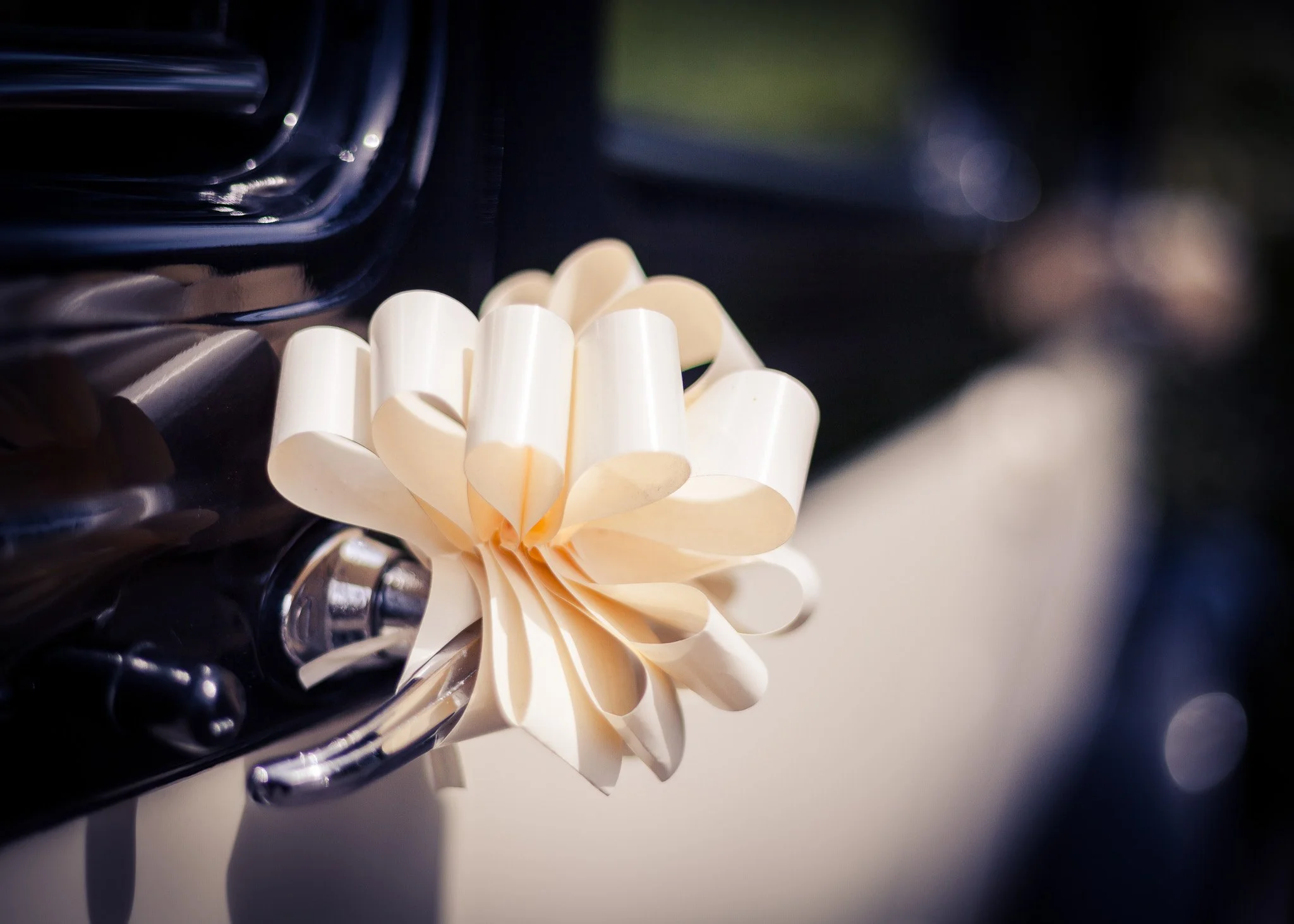 Close-up of a white decorative paper flower surrounded by black glossy objects, reflecting light, set against a dark background.