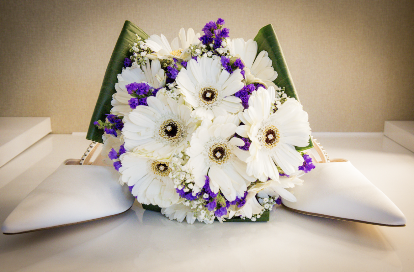A traditional Japanese floral arrangement with white daisies, purple flowers, and green leaves, placed on a white pillow on a table.