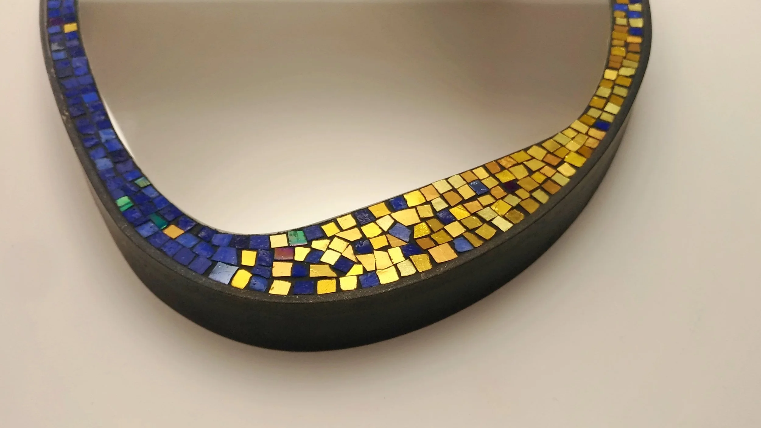 Miroir rond entouré de mosaïque en carreaux de verre bleus et dorés.