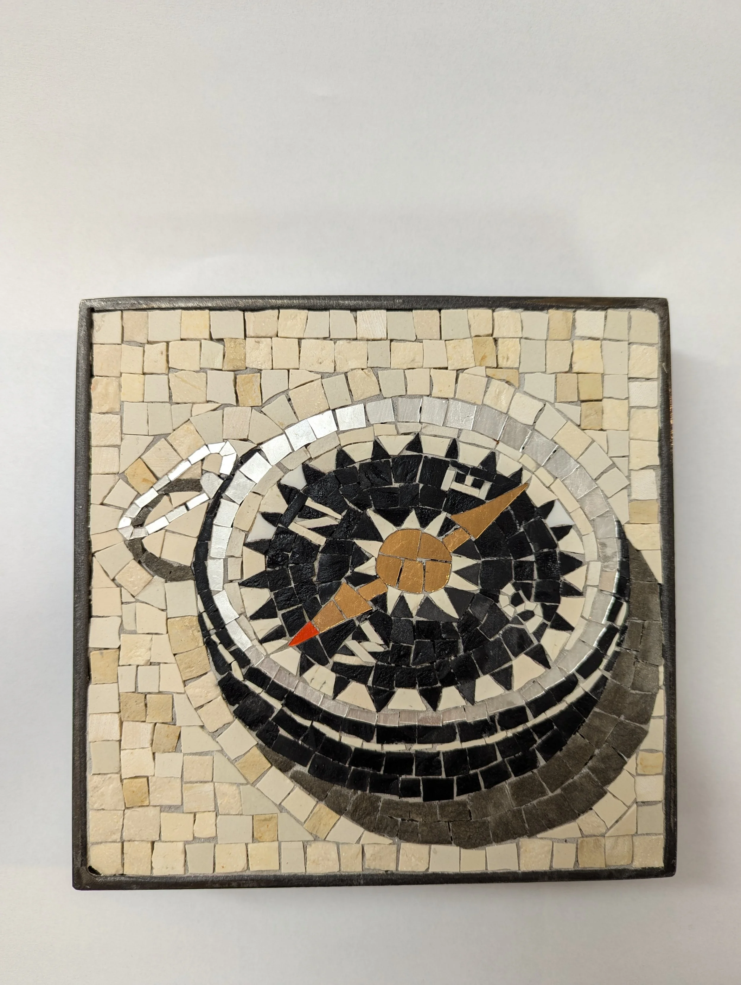 Tableau en mosaïque en forme de boussole avec un fond beige et un centre noir, dans un cadre gris.