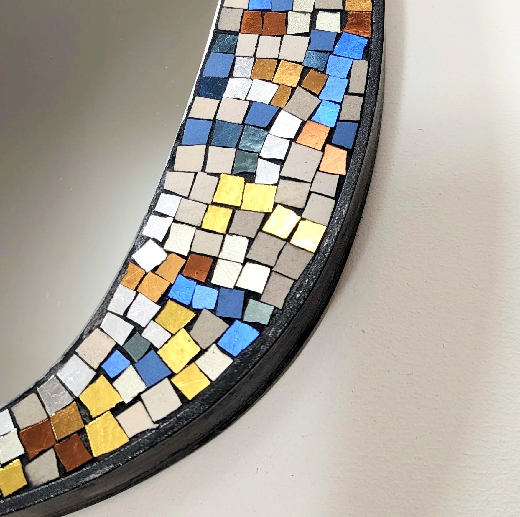 Détails d'un miroir en mosaïque coloré, avec des carreaux de différentes couleurs comme le blanc, le bleu, le jaune, le orange, le marron et le gris, encadrée en noir.