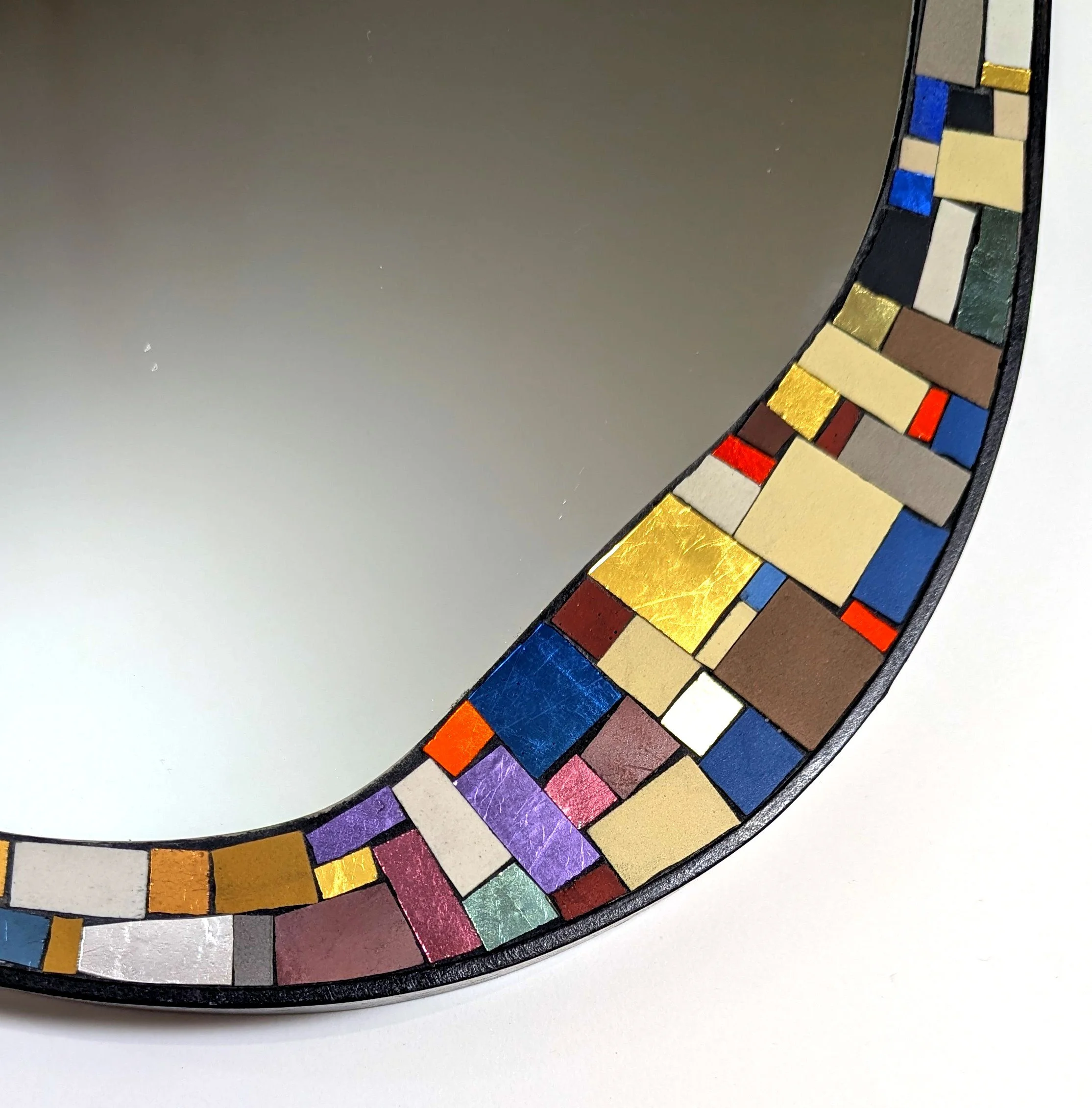 Détail d'une œuvre d'art en mosaïque avec des tuiles colorées comme le doré, le rouge, le bleu, le vert, le violet, le noir et le beige, disposées en un motif circulaire ou en arc.
