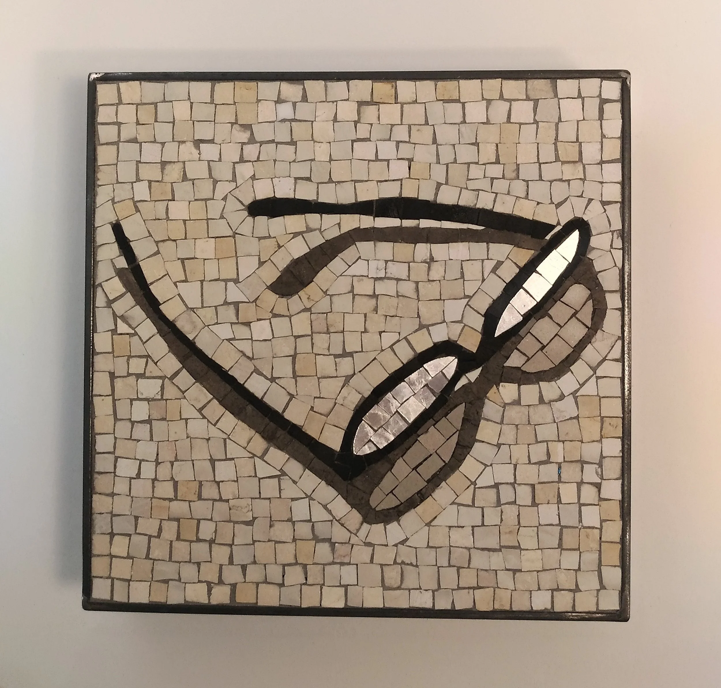 Une mosaïque de style art déco présentant une paire de lunette avec une ligne noire sur un fond beige et une forme noire en haut à droite.