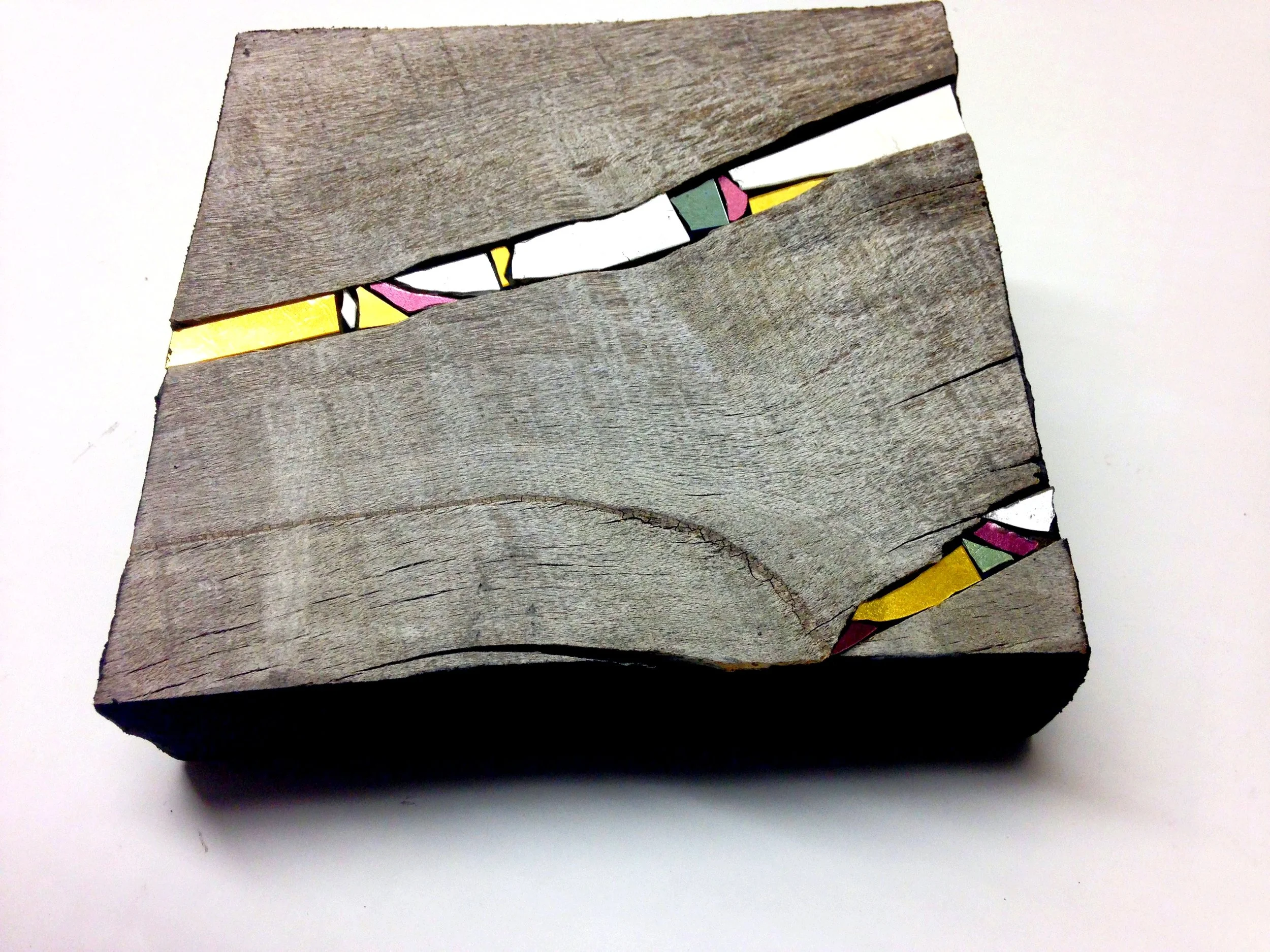Bois avec des morceaux colorés de verre ou de céramique en dessous, partiellement caché par deux planches de bois grisâtre